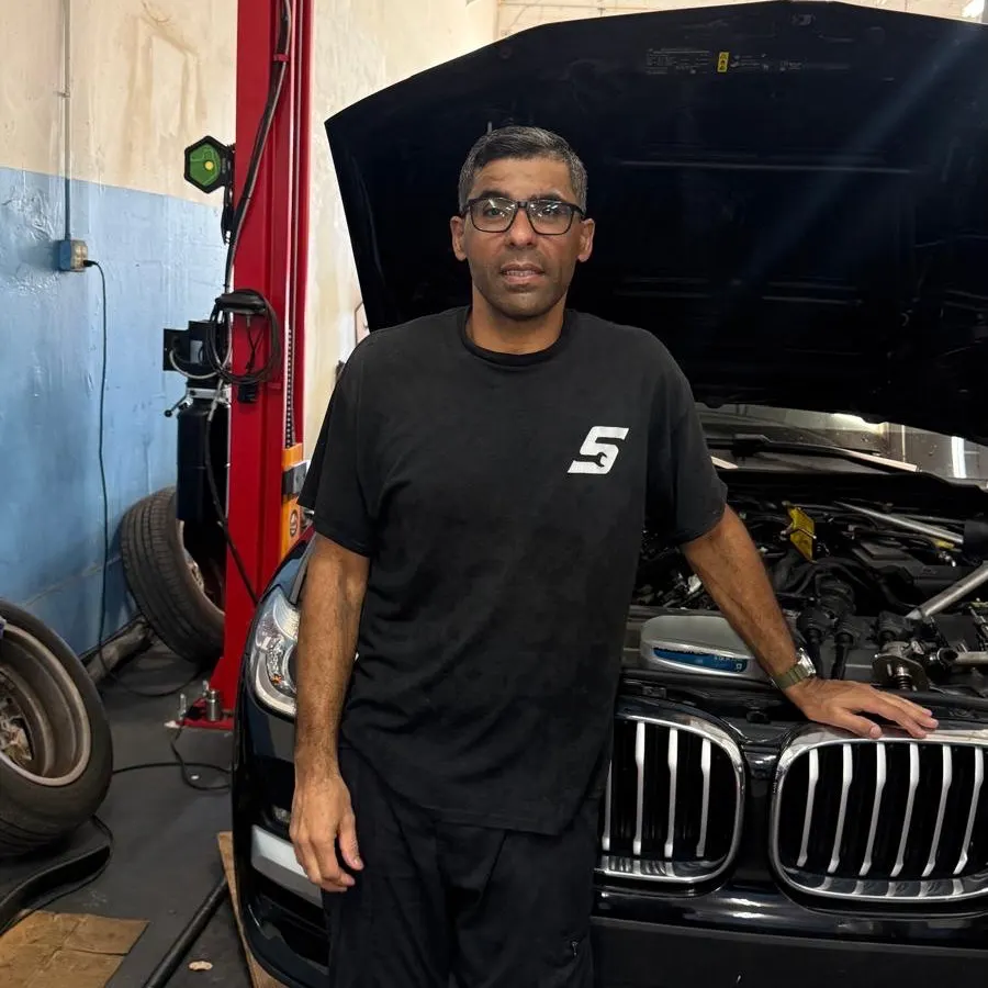 Sandro, owner and mechanic, standing next to a BMW with the hood open at Phil's Electric Auto Expert